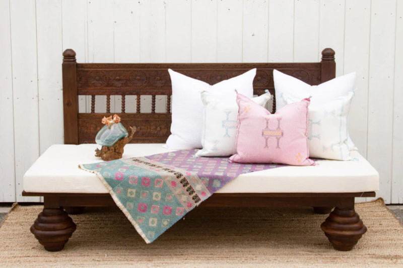 Slatted wood daybed couch with a white cushion, shown from the front with pillows and a throw across the seat.