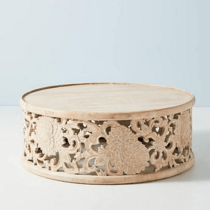 Solid wood cocktail table in a light natural finish, front view showing floral fretwork and a round raised rim.