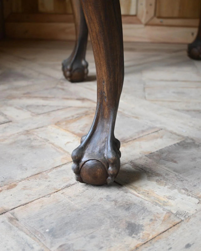 Solid wood cocktail table shown close-up at a curved leg and its rounded foot resting on the pale floor.