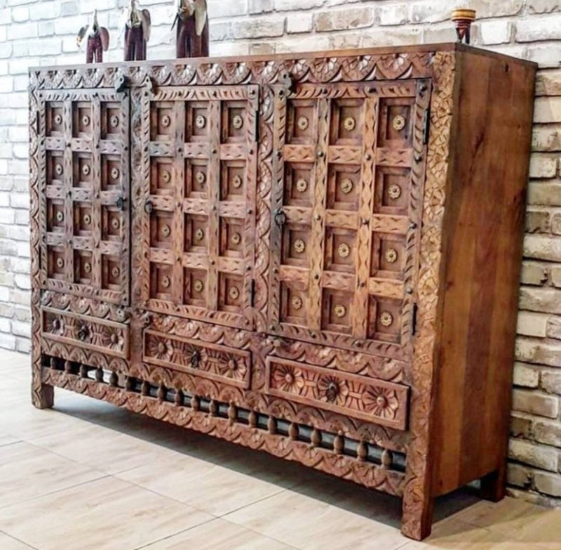 Solid wood paneled buffet in a front view angled from the right, showing rustic carved doors and three floral drawers.