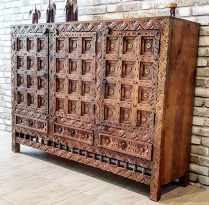 Solid wood paneled buffet in a front view angled from the right, showing rustic carved doors and three floral drawers.