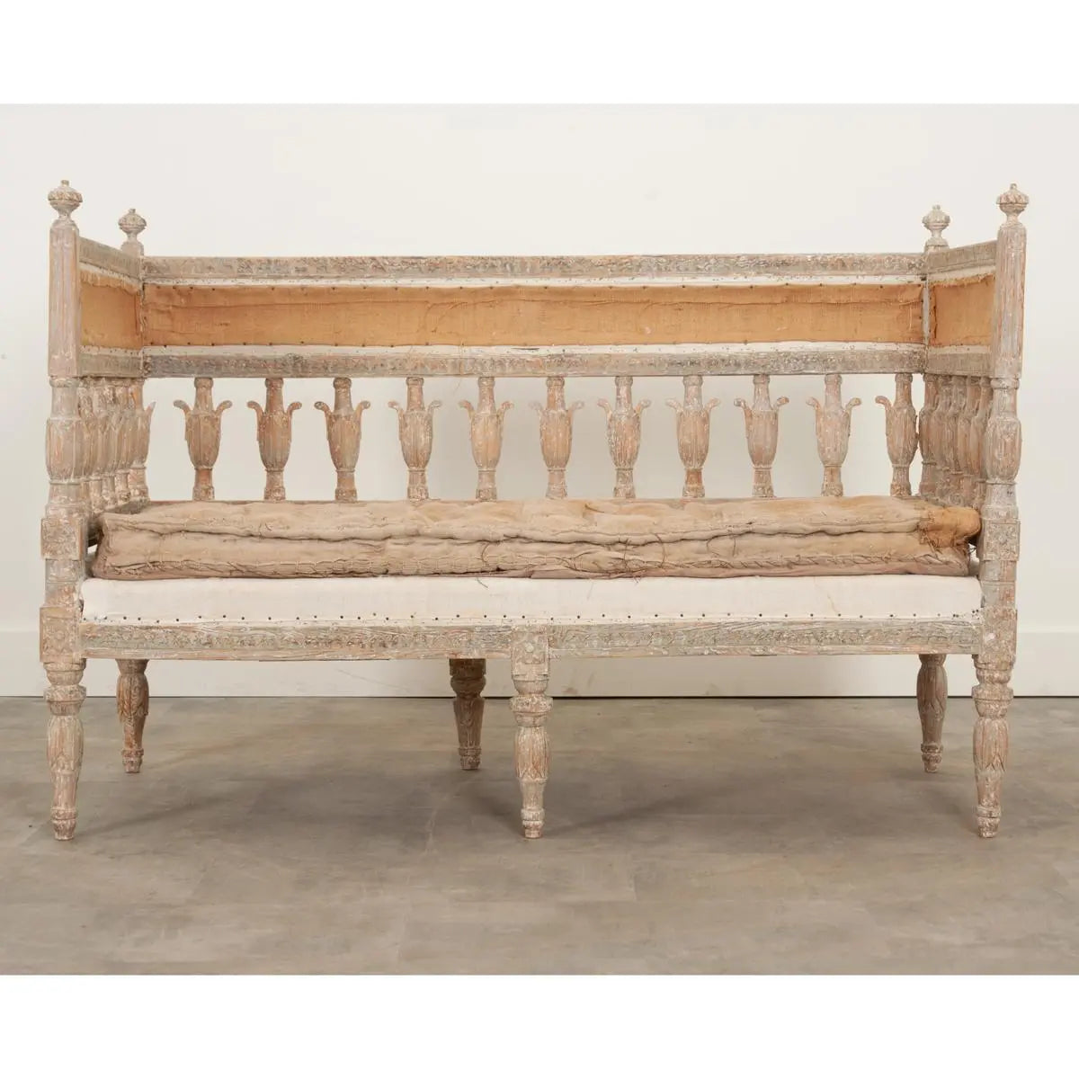 Spindle back bench in a light wood finish with a cream cushion, front view showing its full frame and turned legs.