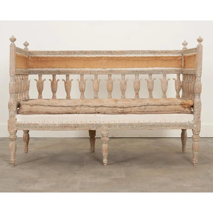 Spindle back bench in a light wood finish with a cream cushion, front view showing its full frame and turned legs.
