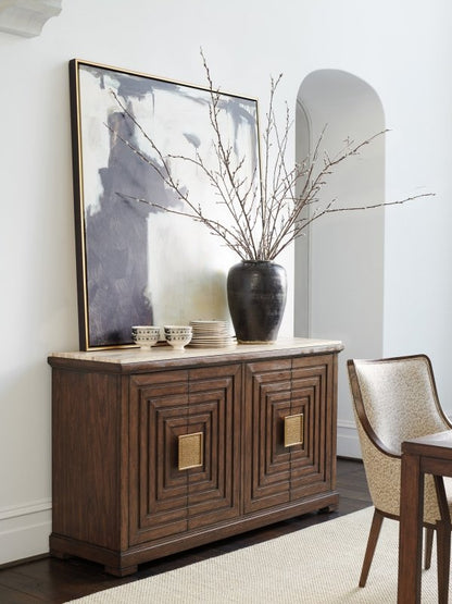 Stone top credenza in walnut wood, front view with closed carved doors, stacked dishes and a dark branch-filled vase.