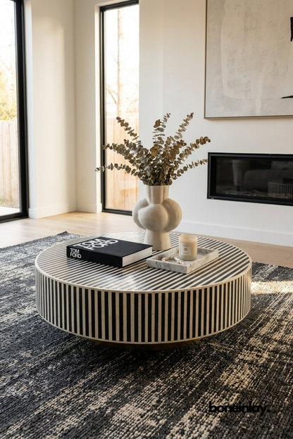 Handcrafted striped bone inlay round coffee table styled in a modern living room with brass base, eucalyptus vase, and Tom Ford book on a dark textured rug