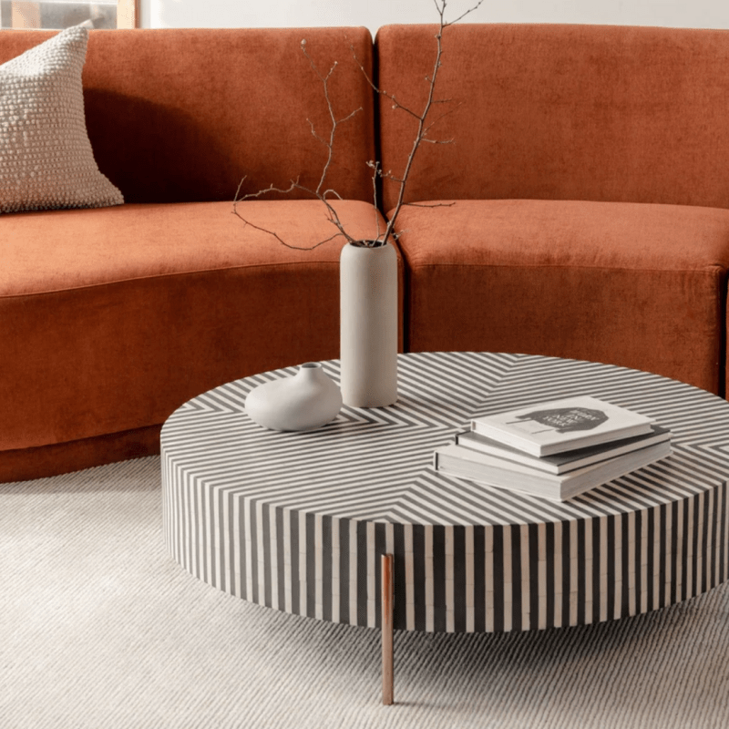 Handcrafted black and white striped bone inlay round center table with slim brass metal legs placed in front of an orange sectional sofa