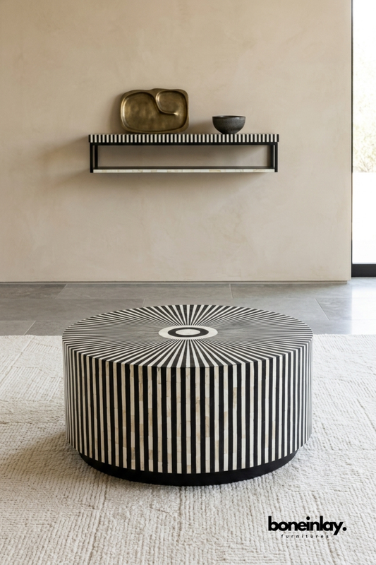Round bone inlay coffee table featuring a bold radiating sunburst pattern in contrasting black and white stripes. Bold graphic design wraps seamlessly from tabletop to drum-style base. Styled beneath a matching bone inlay wall shelf with a brass dish and ceramic bowl. A dramatic statement coffee table for modern and eclectic living spaces.