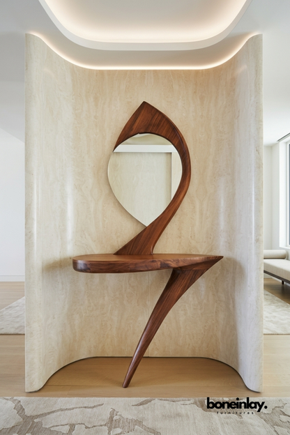 Sculptural solid walnut console table featuring a dramatic curved silhouette and integrated round mirror. Designed as a striking artistic statement piece within a curved travertine wall niche. Rich wood grain and fluid organic form showcase premium craftsmanship. A bespoke entryway console table for luxury and designer interior spaces.