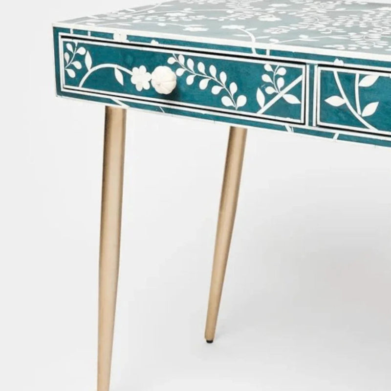 Teal bone inlay desk drawer detail showing white floral vine inlay pattern, carved bone flower drawer knob, and slim brass tapered legs on a plain white background