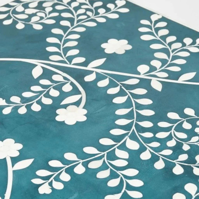 Macro shot of teal bone inlay tabletop surface showing intricate white hand-laid floral vine and daisy pattern crafted from natural bone on mango wood base