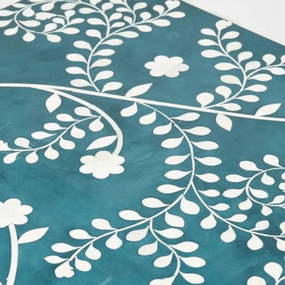 Macro shot of teal bone inlay tabletop surface showing intricate white hand-laid floral vine and daisy pattern crafted from natural bone on mango wood base