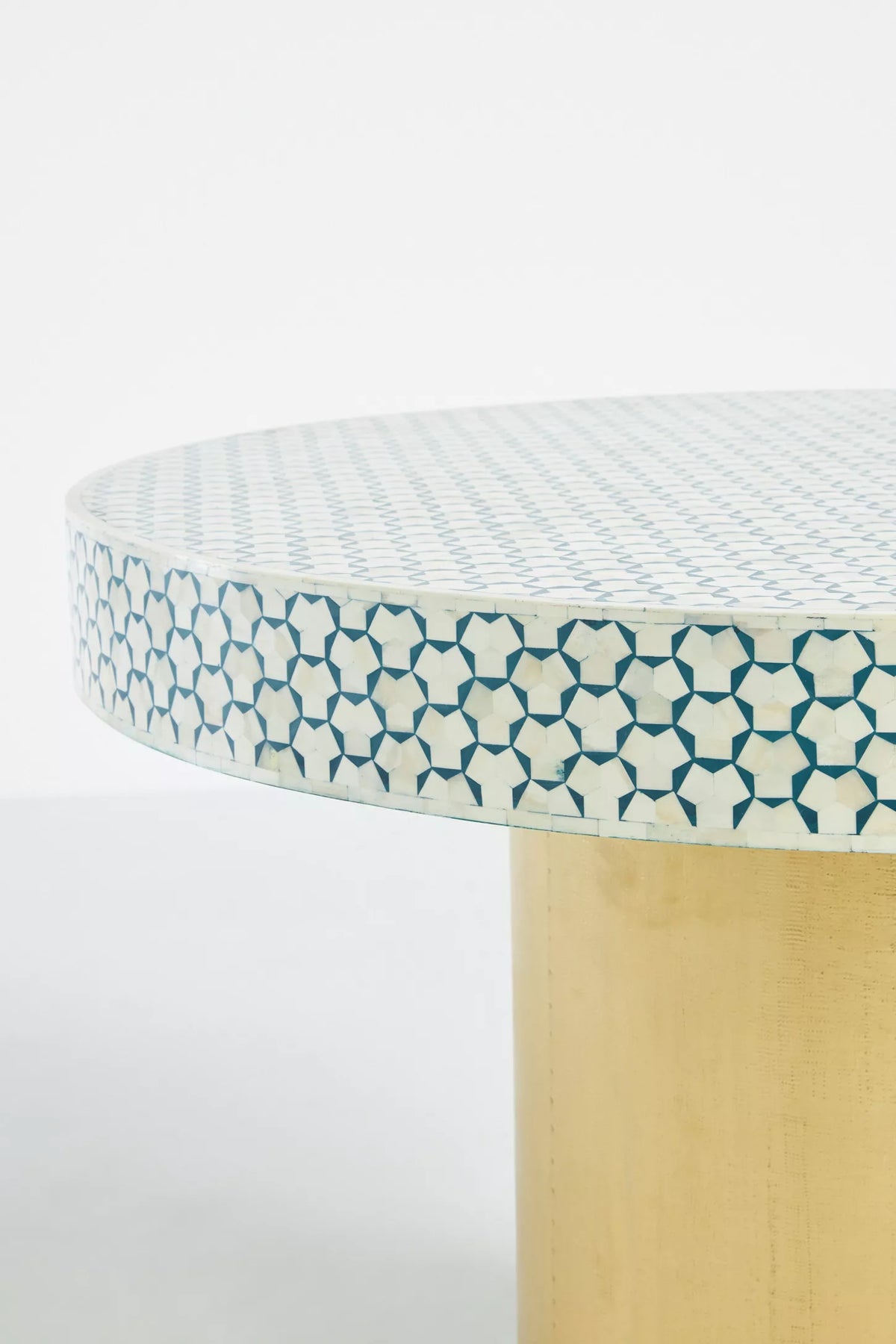 Close detail of teal and ivory geometric bone inlay pattern on round dining table edge with brass pedestal base