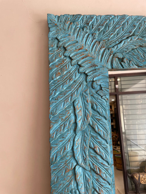 Turquoise carved decorative mirror in wood, corner detail view revealing distressed paint over sculpted leaf relief.