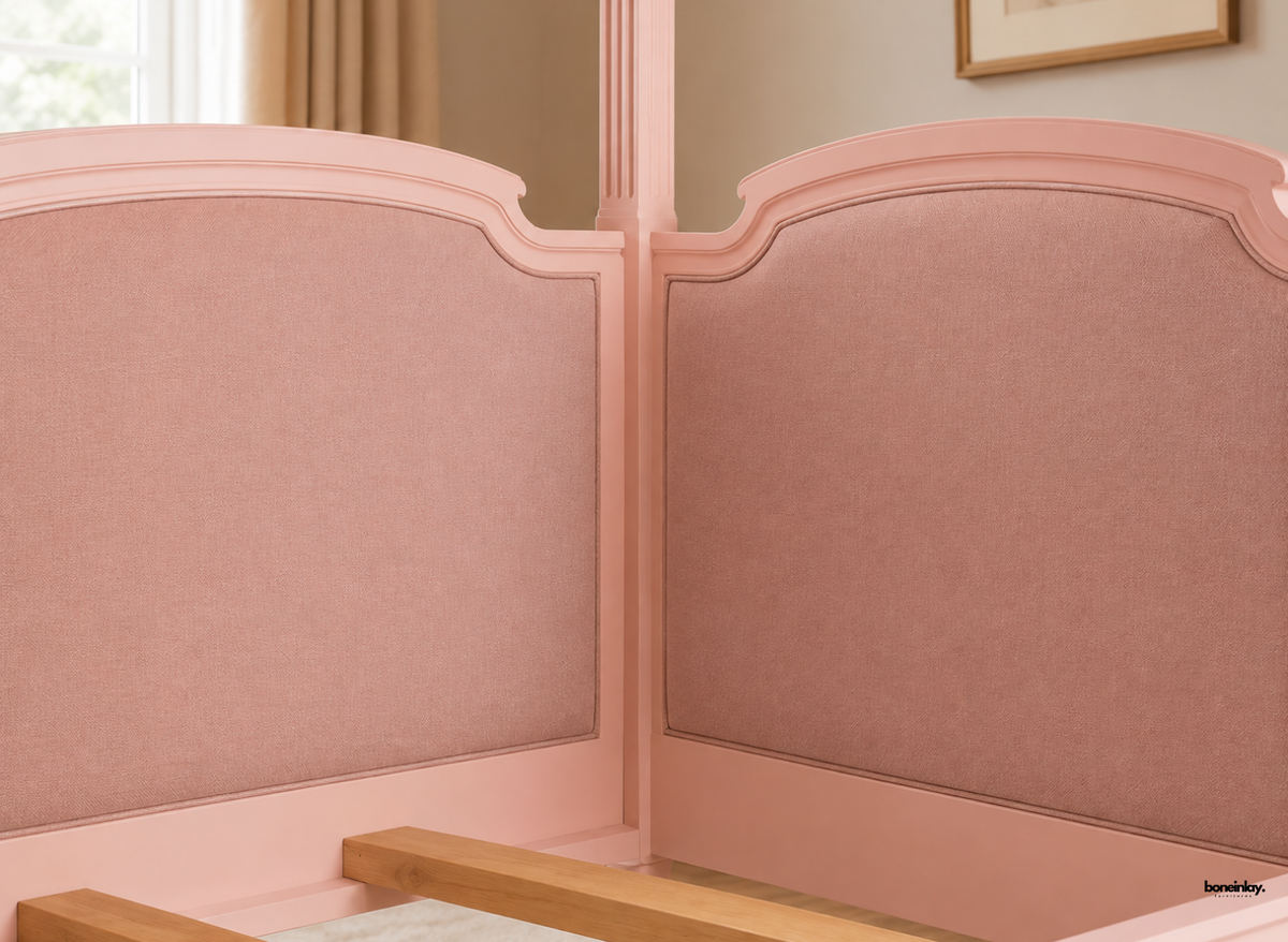 Close-up view of a handmade pink wooden canopy day bed showcasing finely upholstered curved headboard panels and fluted corner posts. This romantic artisan bed combines soft textured upholstery with exquisite craftsmanship for a chic bedroom aesthetic.