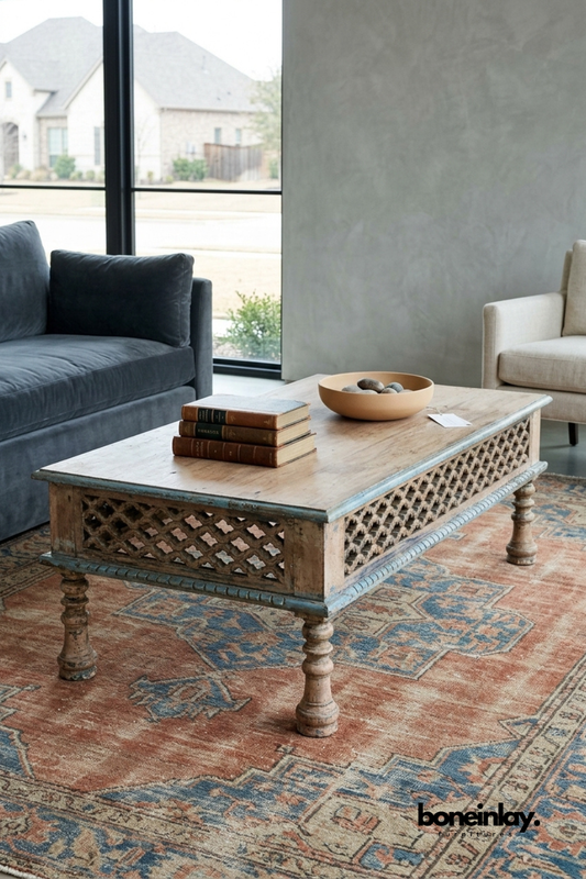 Weathered blue-grey coffee table featuring a hand-carved diamond lattice panel along the apron and turned wood legs. Distressed natural wood top contrasts with the softly painted base for vintage character. Styled with a stack of leather-bound books and a wooden bowl of stones on a Persian rug. A charming statement coffee table for traditional and eclectic living rooms.