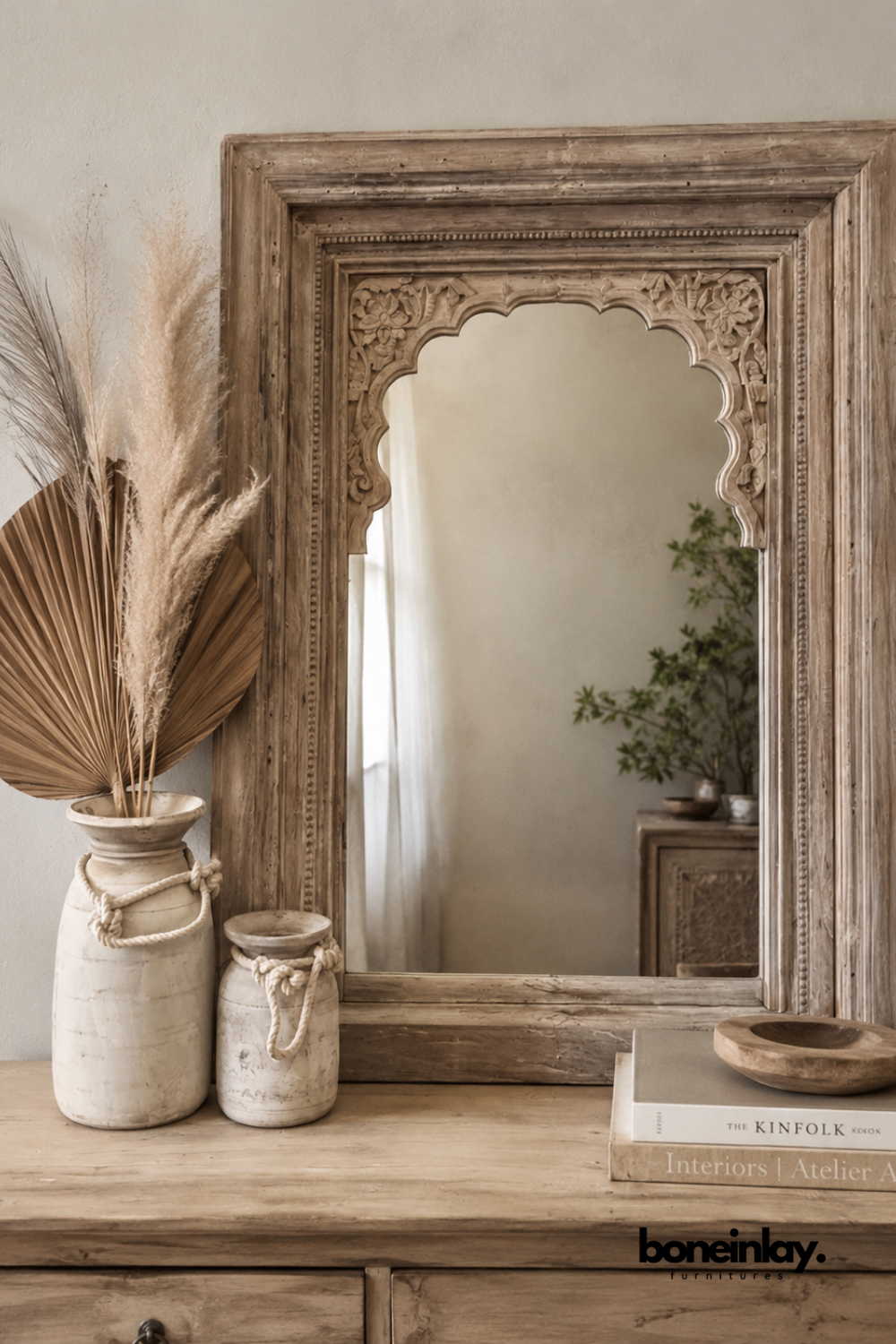 Natural wood mirror with an arched, scalloped carved frame top.
Hand-carved floral detailing decorates the upper corners.
Warm, weathered wood tone adds a vintage, artisanal character.
Styled on a wood dresser with ceramic vases and dried pampas grass.