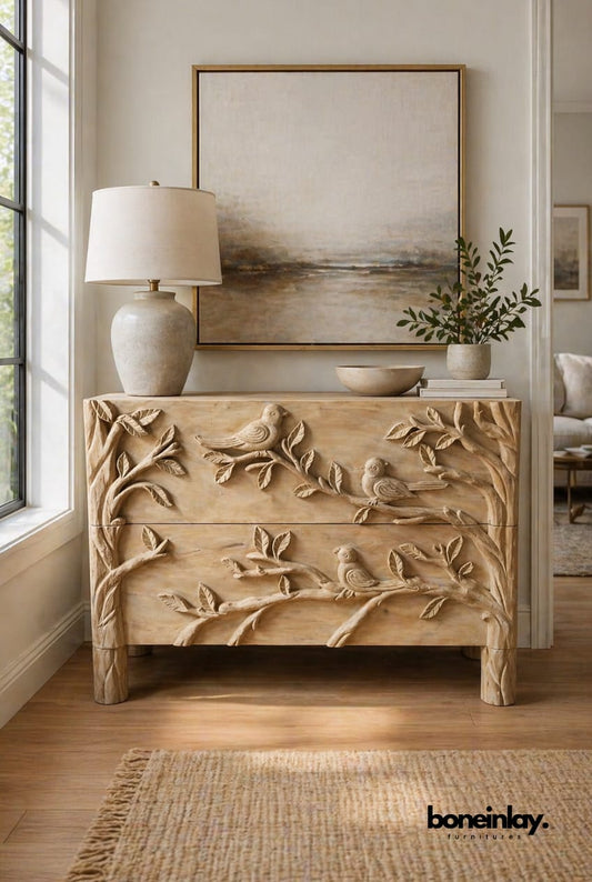 A 2-drawer solid wood dresser featuring a high-relief hand-carving of birds on tree branches across the front and sides in a light finish.