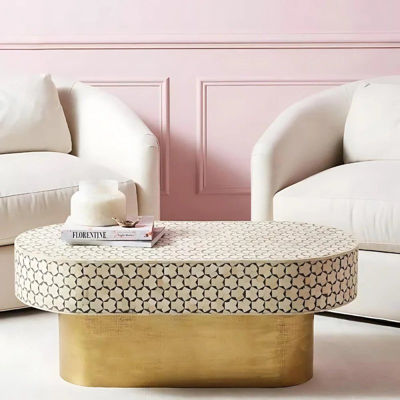 White bone inlay oval cocktail table with charcoal geometric pattern and brass base, styled front view in a living room