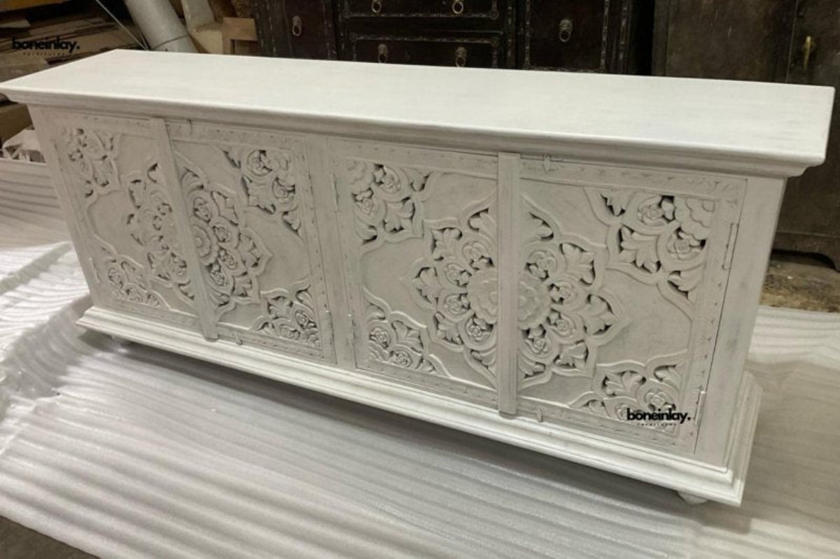 White wood cabinet in an angled view, showing the carved doors, long top and one end of the piece.