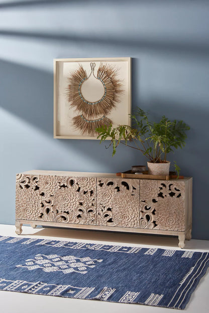 Whitewash Lotus Sideboard in wood, shown front-on against a slate blue wall with four carved cabinet doors.