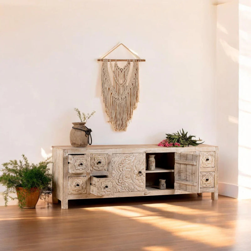 Whitewashed wood credenza styled in a living room, with decor on top and its carved doors and drawers visible.