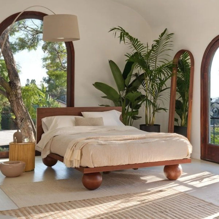 Agneta modern solid wood platform bed frame featuring four thick sculptural round sphere ball feet and a sleek low-profile headboard in a bright bedroom setting.