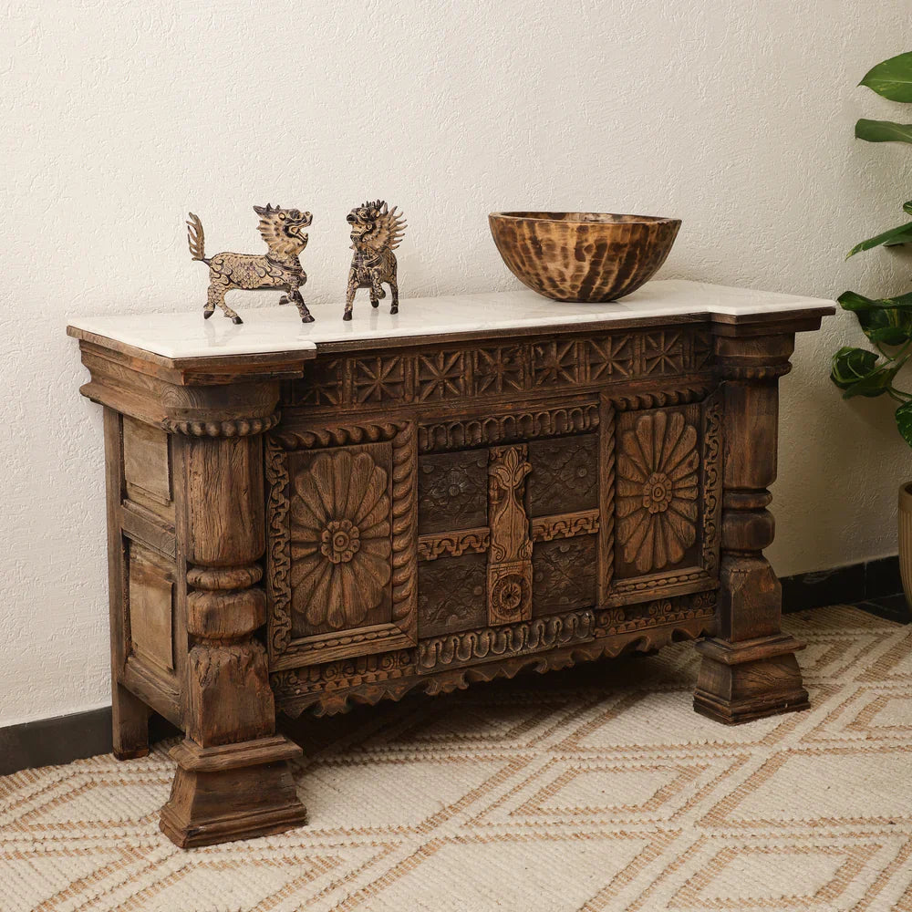 Antique carved wooden credenza styled with two decorative figurines and a bowl on its light-colored top.