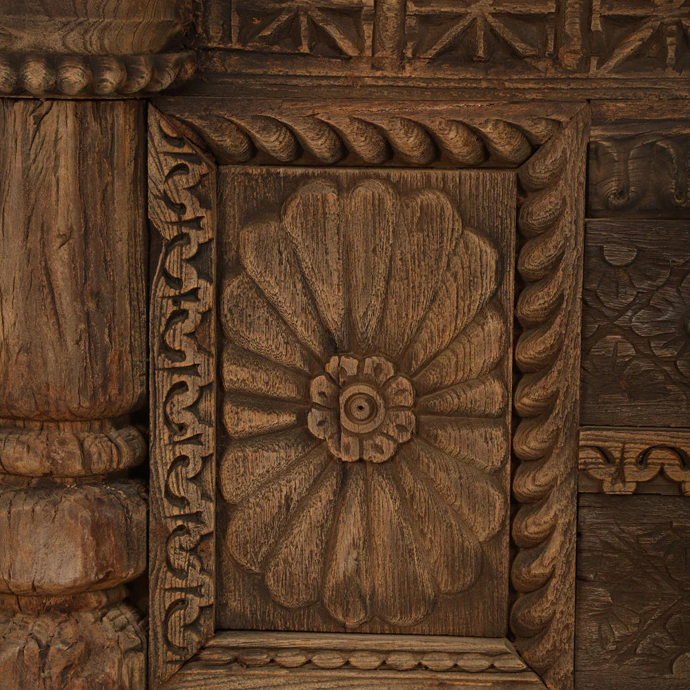 Close-up of a floral carving and twisted border on the antique wooden credenza, showing its textured brown finish.