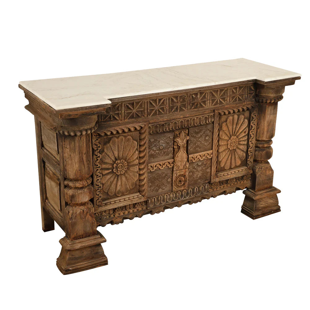 Antique carved wooden credenza viewed from the left, showing its paneled side, light-colored top, and substantial column legs.