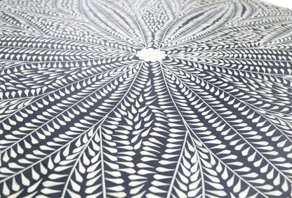 Close-up of ivory bone inlay leaves radiating from a floral center on the black dining tabletop.