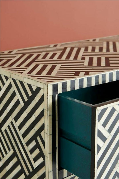 Angled top and side view of a black and white optical bone inlay dresser showing the geometric parquet-style inlay on the top surface and an open teal-lined drawer interior.