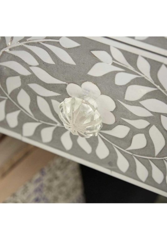 Close-up of grey bone inlay dresser drawer corner with flower-shaped knob and white leaf inlay pattern on grey surface