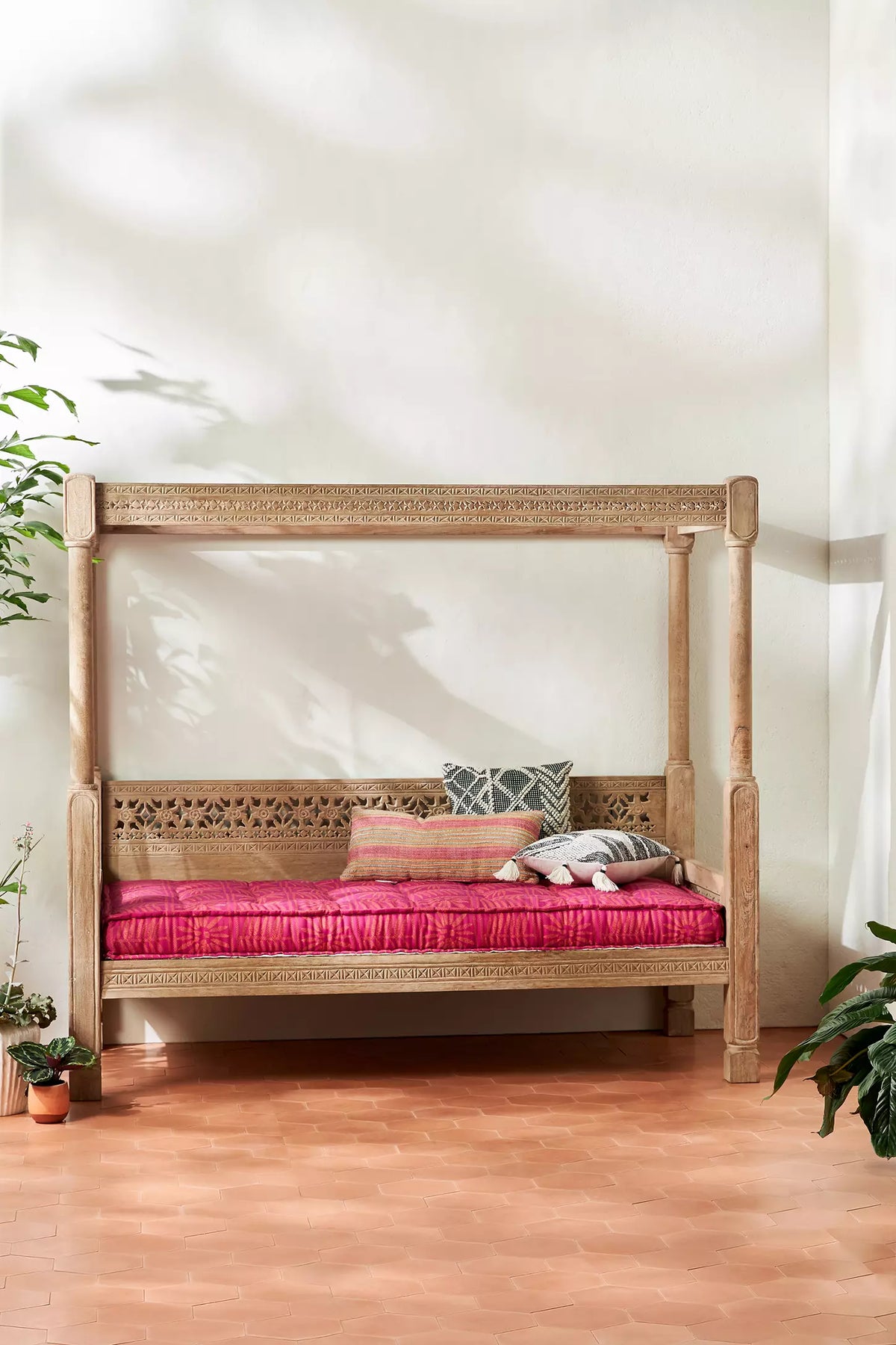 Natural-finish solid wood Ezana canopy daybed with intricate lattice backrest, pink cushion, and patterned tile floor.