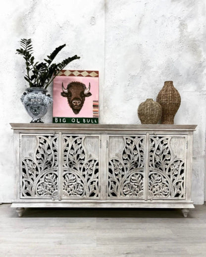 Front view of an Indian hand-carved white wooden buffet sideboard with four doors featuring elaborate floral and leaf patterns in a distressed white finish.