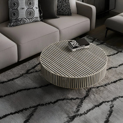 A round coffee table featuring a sophisticated black and white vertical striped bone inlay pattern, styled in a modern living room setting.