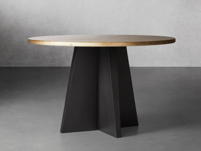 A luxury round dining table with a hand-embossed recycled brass tabletop and a sculptural black iron vertex pedestal base.