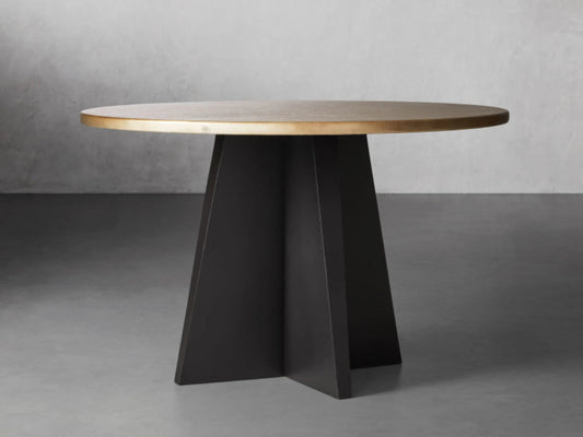 A luxury round dining table with a hand-embossed recycled brass tabletop and a sculptural black iron vertex pedestal base.
