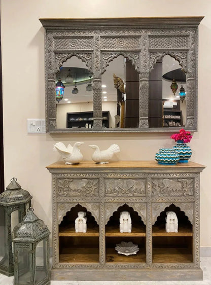 Gray carved wooden jharokha wall mirror with three scalloped arches and floral detailing, displayed above a matching console.