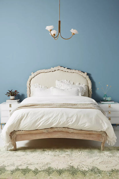 Hand-carved Menagerie bed frame in whitewashed mango wood with neutral linen upholstered headboard, styled in an airy bedroom.