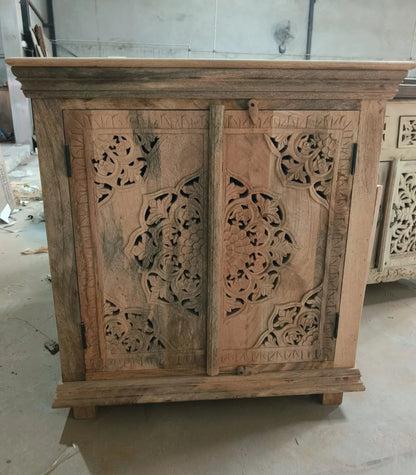 Close-up of a natural wood sideboard featuring intricate hand-carved floral mandala patterns on two doors with visible wood grain and traditional latch.