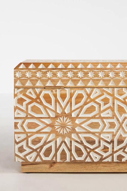 Floral carved storage trunk, close-up of the swirling pattern across its front and the border at its base.