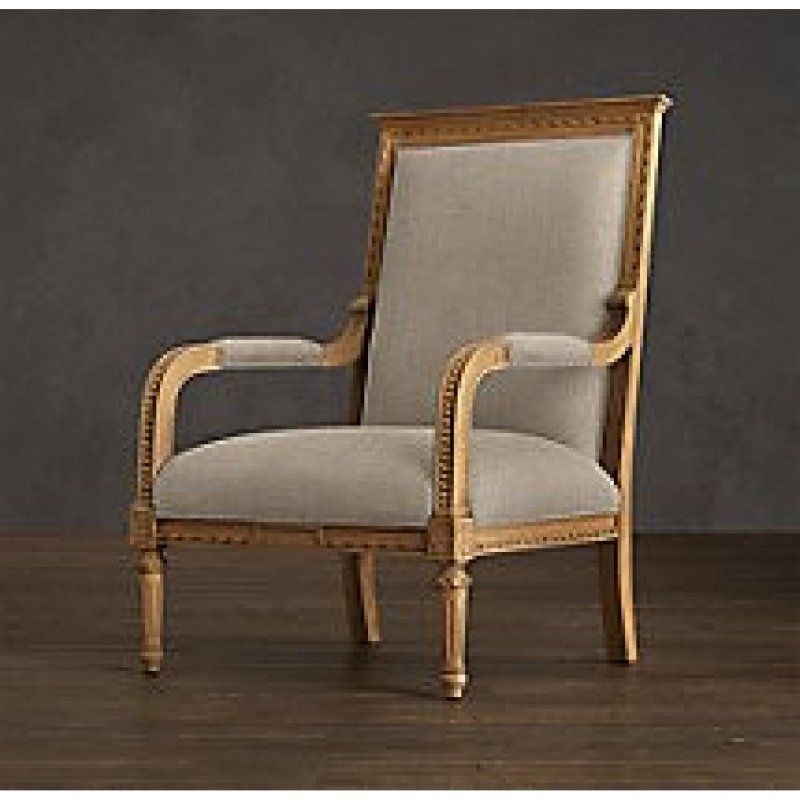 A side-angle view of a luxury Louis XVI style bergère chair with a gilded solid wood frame and neutral linen upholstery against a dark backdrop.