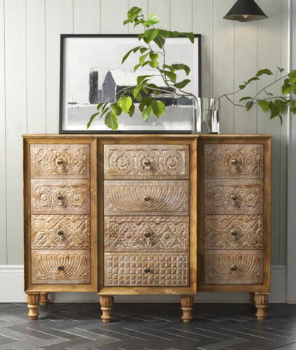 Vertical 12-drawer solid wood dresser with diverse hand-carved geometric patterns on each drawer and turned spindle legs in a modern interior.