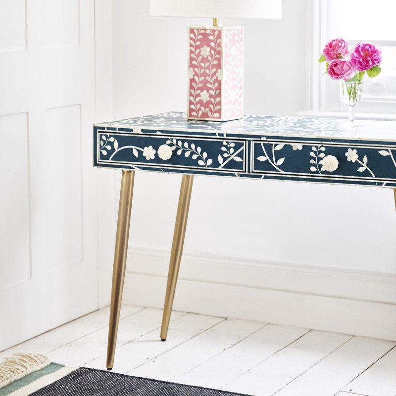 Blue floral bone inlay console desk with white vine and rose pattern on drawers, brass legs, styled with a pink floral table lamp and fresh roses in a white-panelled room