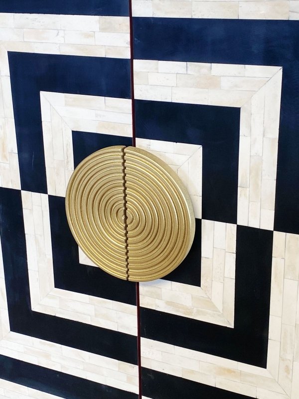 Brass circular concentric ring door knob on bone inlay bar cabinet door with black and white square geometric optical illusion inlay pattern on mango wood body
