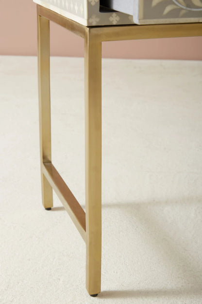 Close detail of slim brushed brass metal legs and base frame of a handmade bone inlay floral nightstand, showcasing precision metalwork and clean minimalist design.