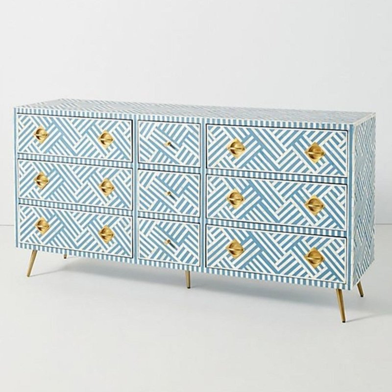 Angled lifestyle view of a blue and white optical bone inlay 9-drawer dresser with brass pulls, showcasing the geometric stripe pattern and slim gold legs in a styled interior.