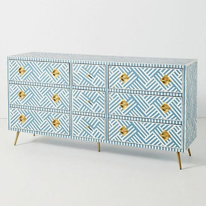 Angled lifestyle view of a blue and white optical bone inlay 9-drawer dresser with brass pulls, showcasing the geometric stripe pattern and slim gold legs in a styled interior.