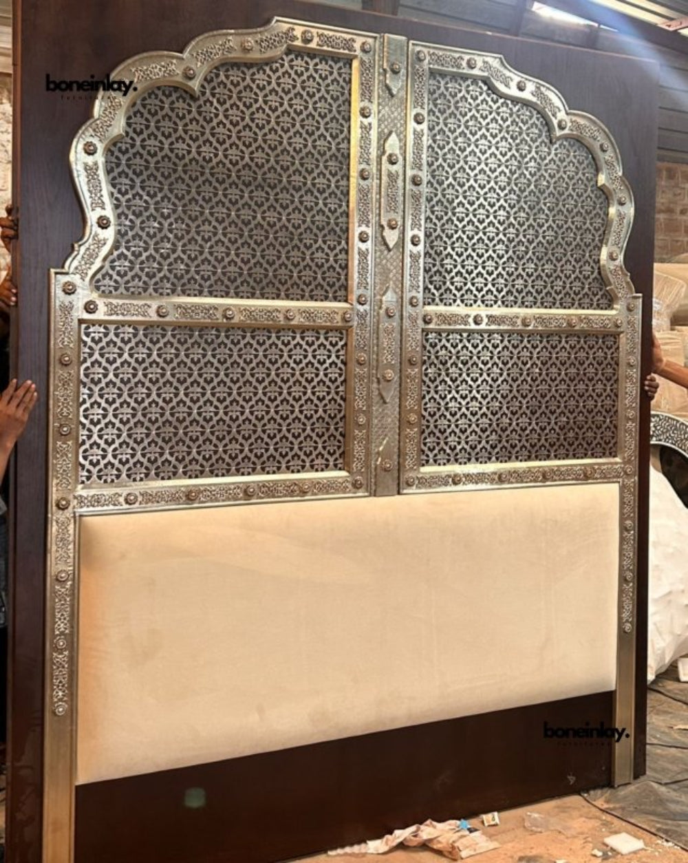 Antique silver hand-embossed metal arched headboard with intricate floral patterns and a cream upholstered lower panel in a modern bedroom setting.