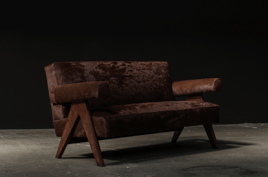 Angled front view of a brown Pierre Jeanneret-inspired sofa showing textured upholstery, padded arms and wooden leg supports.